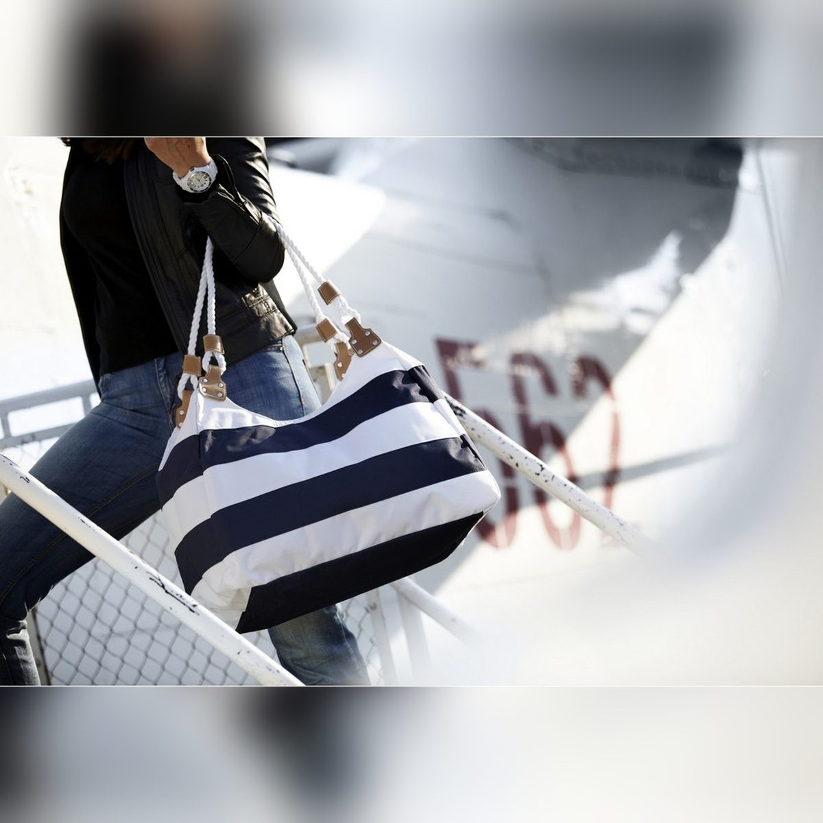 Riviera Stripe Tote carried on the shoulder by a person walking outdoors, showing its navy and white stripes, white rope handles and size when worn.