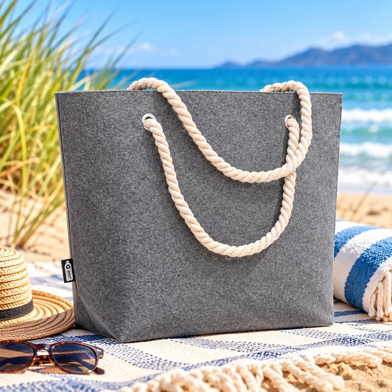 Ocean Felt Tote in grey recycled felt with natural rope handles on a sunny beach.